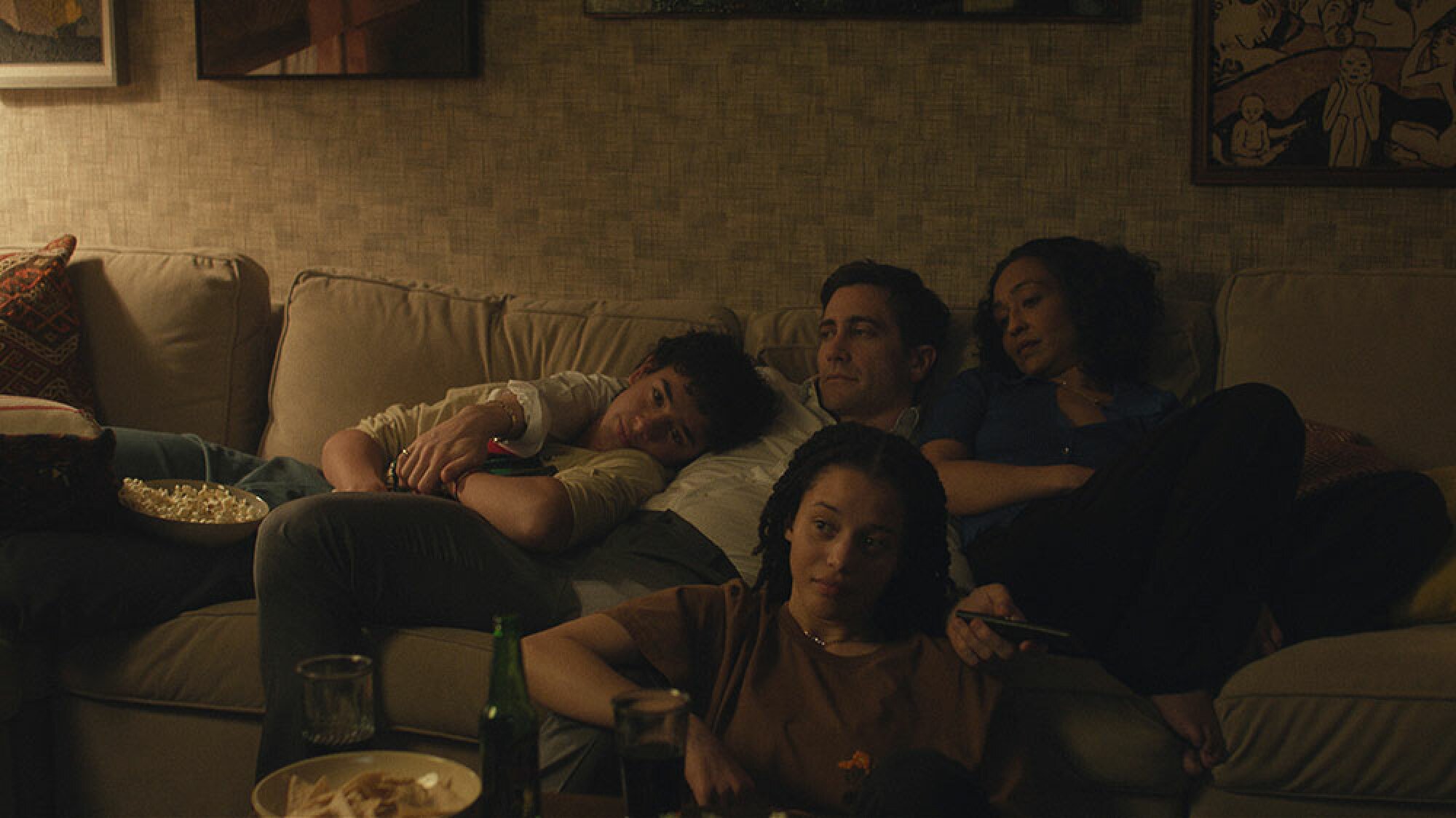 A family consisting of a man, woman, teenage boy and teenage girl sit together on a sofa in the semi-dark.