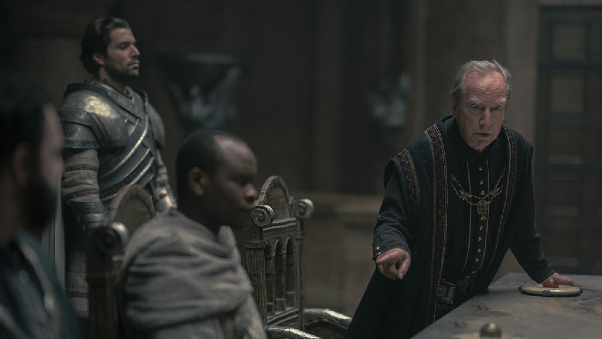 Men stand around a table wearing medieval clothing.