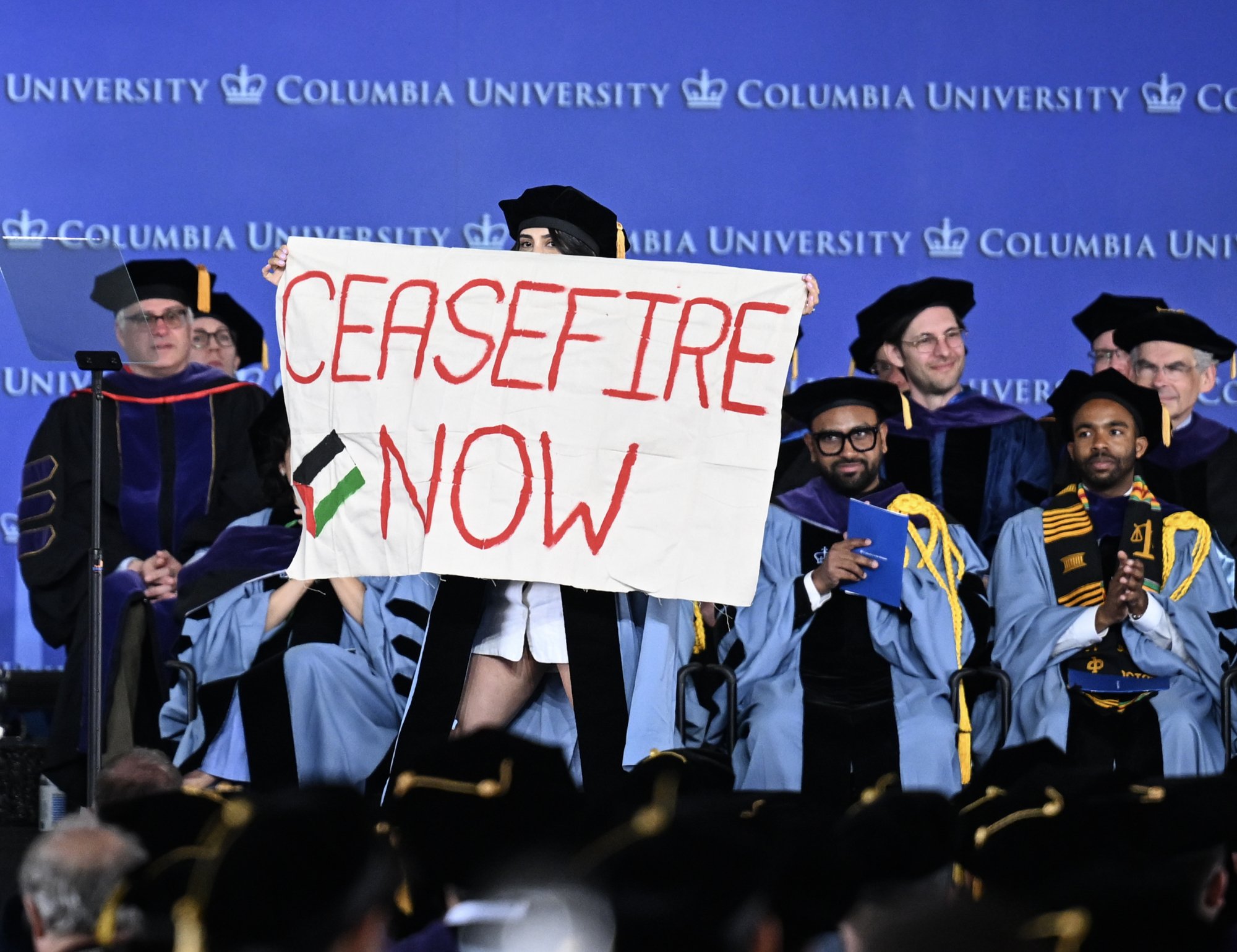 A Columbia University graduate carries a "Ceasefire Now" banner across the stage at graduation.