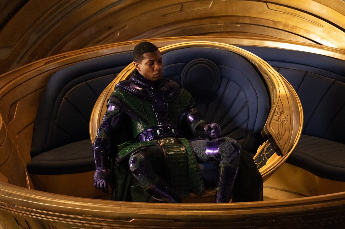 Jonathan Majors as Kang the Conqueror sits in a golden throne wearing purple and green armor.