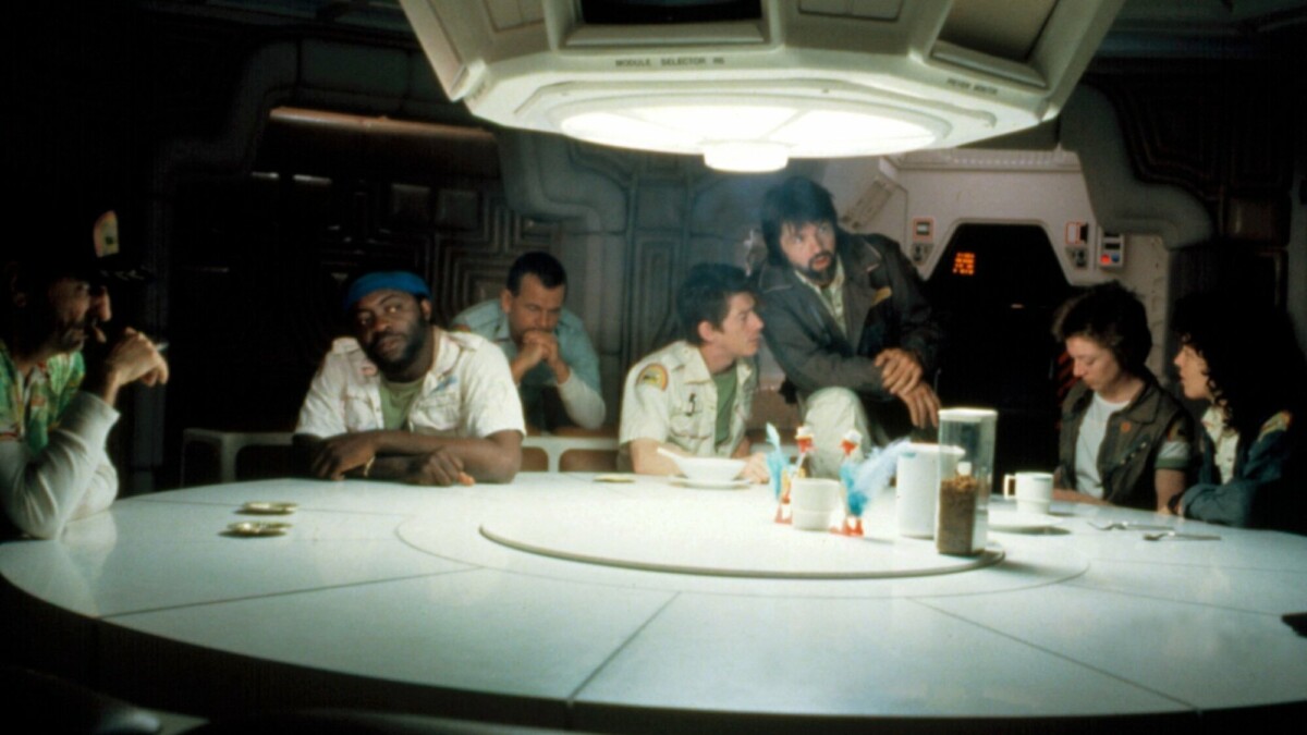 The "Alien" cast sits around a dining room table in a spaceship set.