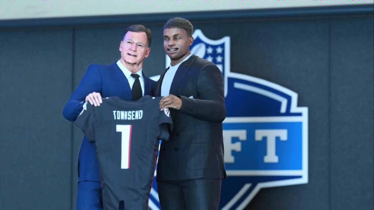 The image shows a virtual or video game representation of an NFL draft event. A young man in a suit is standing next to an older man, who is also in a suit. They are both holding up a football jersey with the name "Townsend" and the number "1" on it. The background features a large NFL draft logo. The scene captures the moment when a player is selected and presented with his new team's jersey.