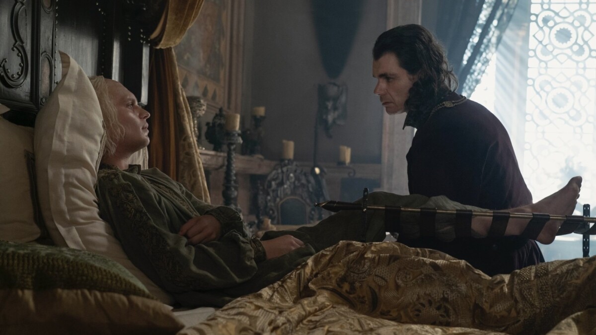 Aegon Targaryen lies in bed with one leg supported in a brace; Larys Strong sits beside him on the edge of the bed.