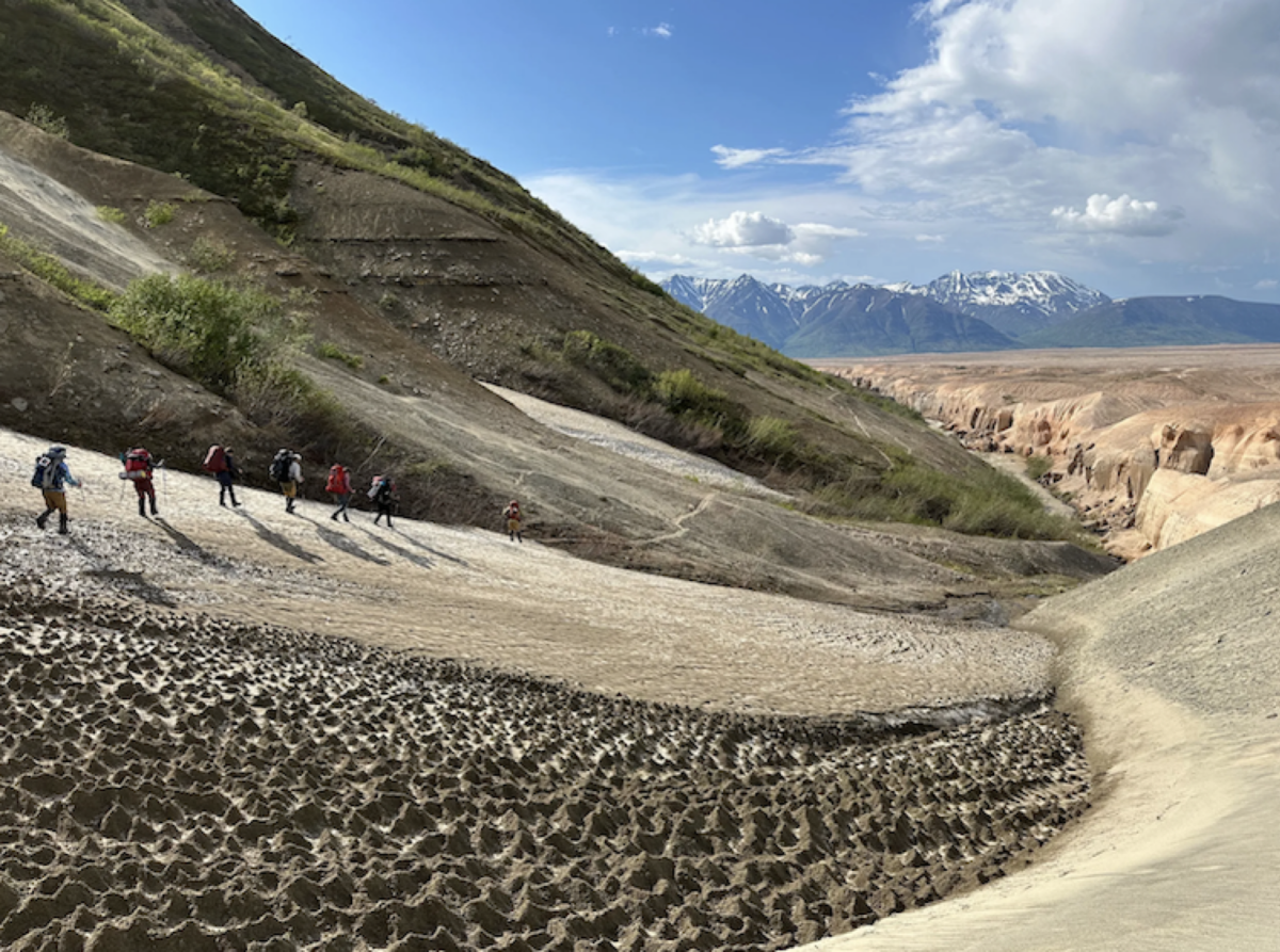 Members of NASA's Goddard Instrument Field Team hiking out of the Valley of Ten Thousand Smokes. The expansive layering of volcanic rock, emitted by Novarupta, is the light pinkish region to the right.