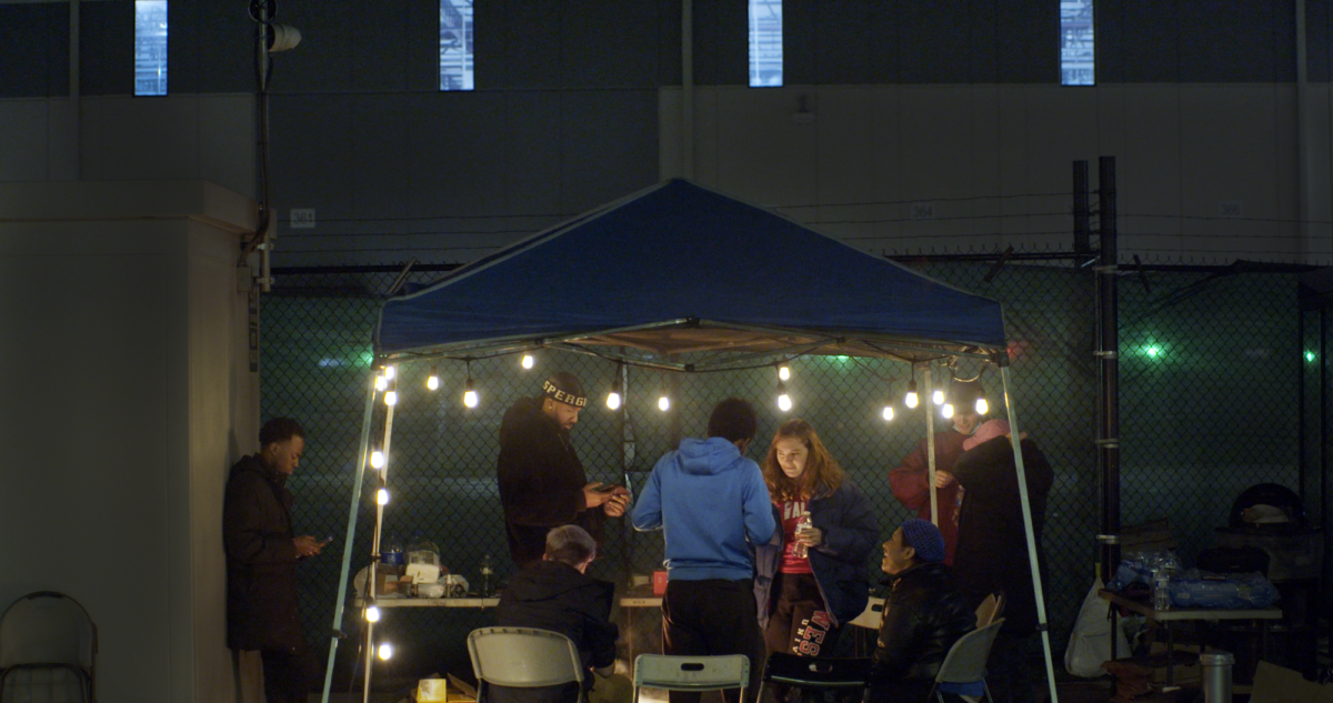 A group of organizers stand under a canopy lit by string lights.