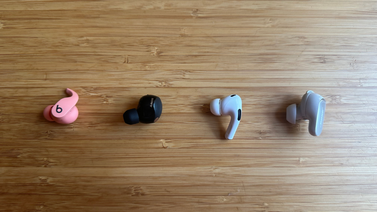 One earbud of the following on a wooden table: Beats Fit Pro, Sony WF-1000XM5, Apple AirPods Pro, and Bose QuietComfort Ultra.