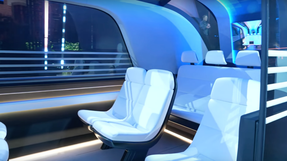 A look inside Tesla's Robovan, showing white seats facing each other and a screen.