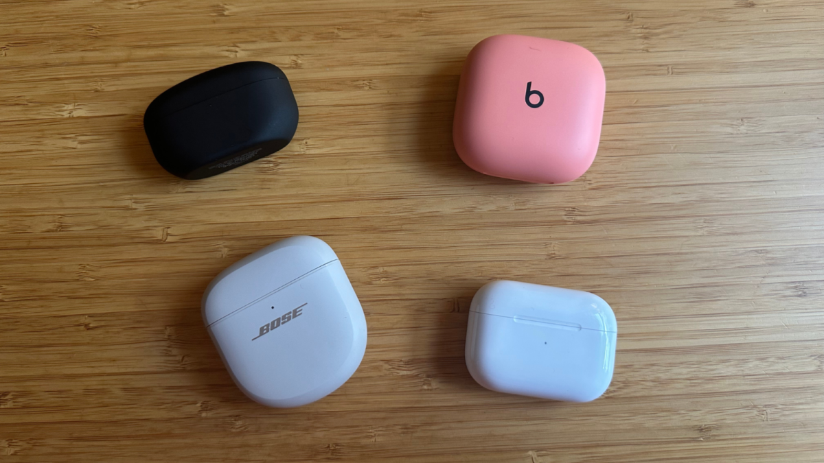 Four earbud cases on a wooden table.