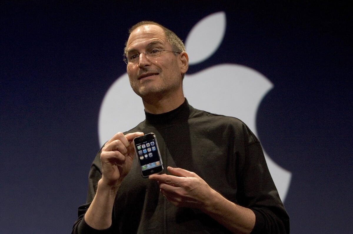 Steve Jobs holding the iPhone in front of an Apple logo. 