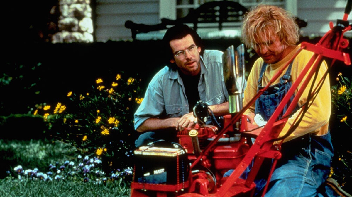 A man crouches beside a man tending to a red lawnmower.