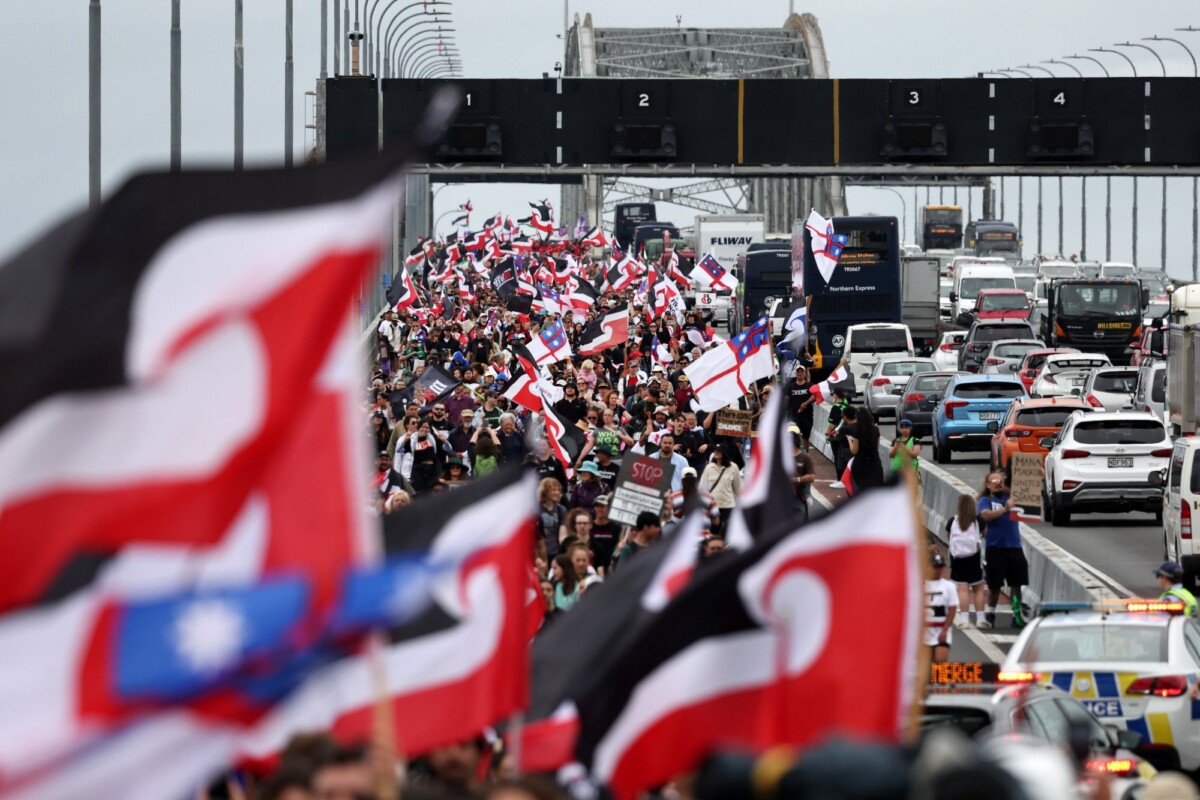 A large group of people holding flags cross over a bridge.