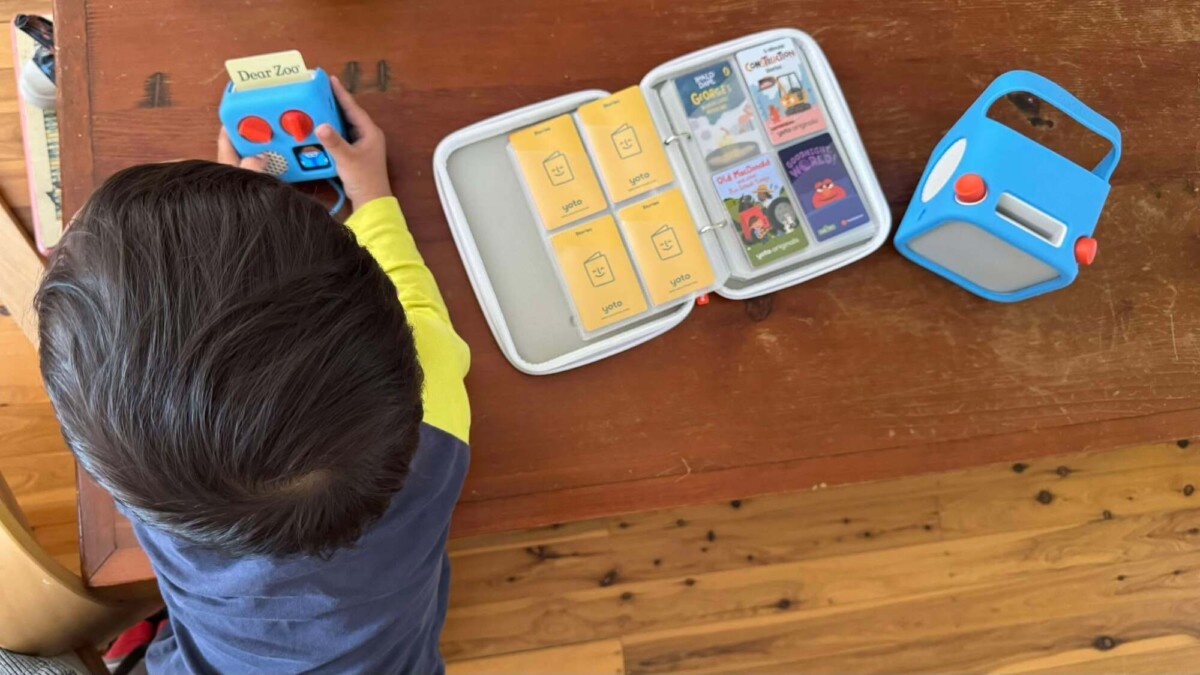 A toddler holding a Yoto Mini, next to a folder of Yoto Cards and a Yoto Player.