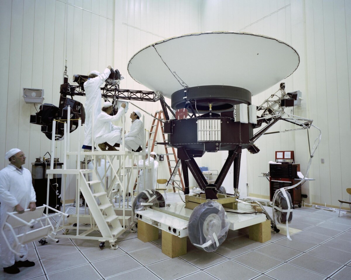 An archival photo of engineers preparing Voyager 1 for launch in a clean room