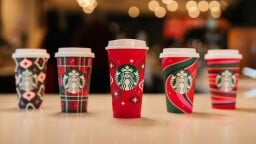 five starbucks red cups with various holiday designs lined up on a counter