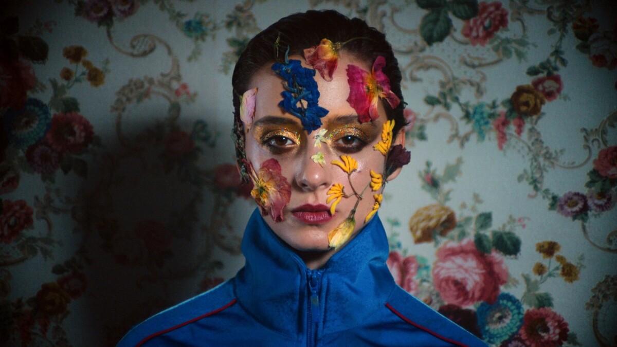 A woman with flowers on her face stares at the camera.