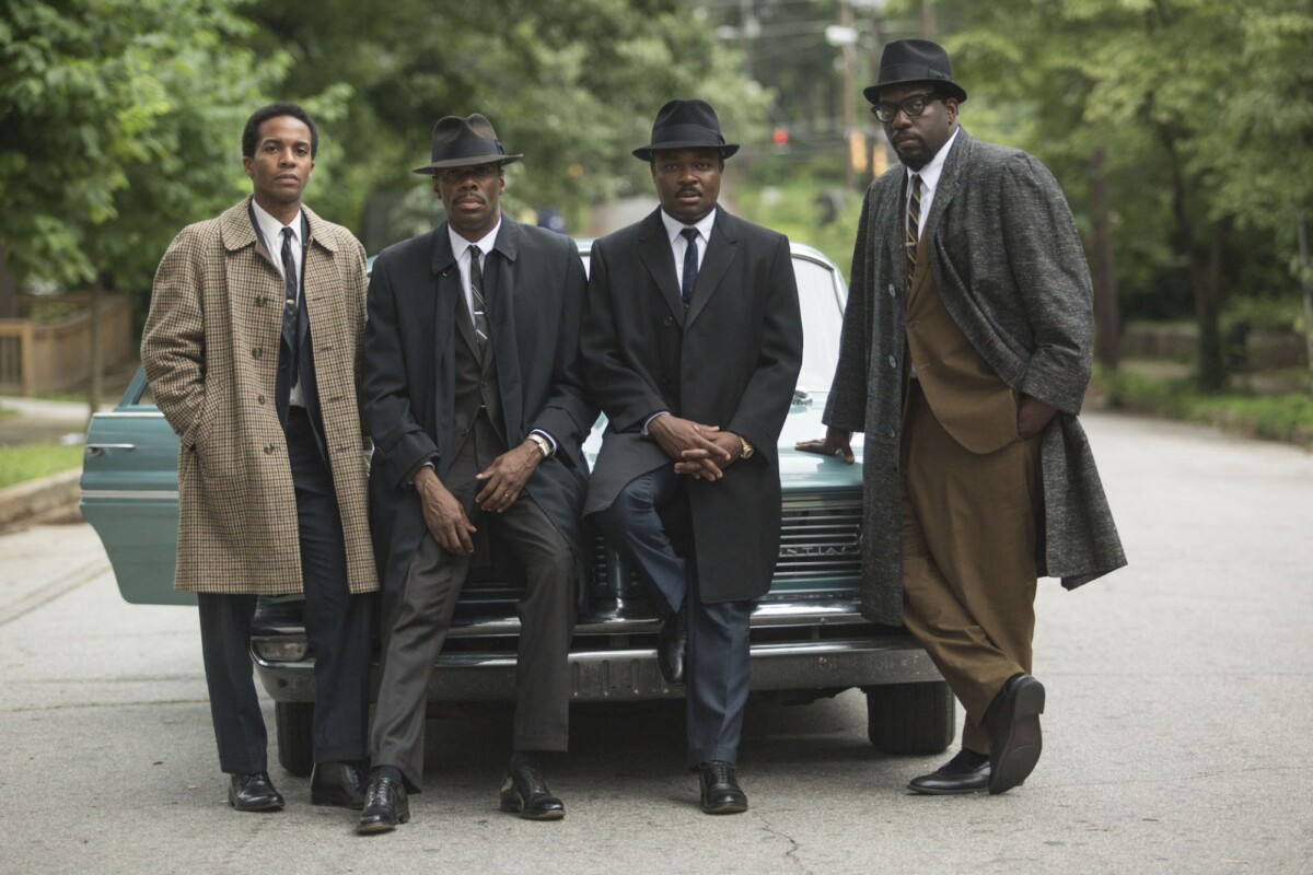 Four Black men in suits pose in front of a car.