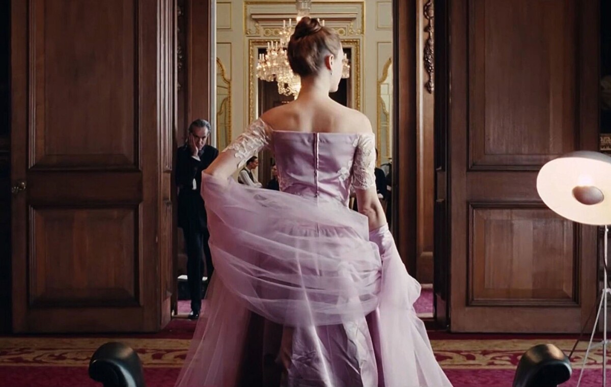 A woman is seen from the back modeling a lavender gown; a man looks at her.