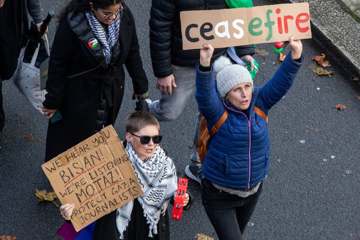 Two people hold up signs during a pro-Palestine march that read "Ceasefire" and "We hear you Bisan! We're listening Motaz! Protect Gaza journalists!"