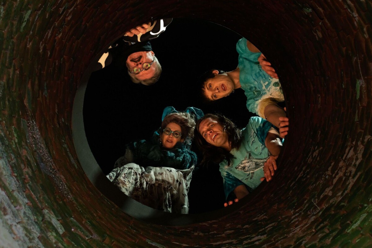 A group of people cluster around the edge of a sewer hole, looking down.