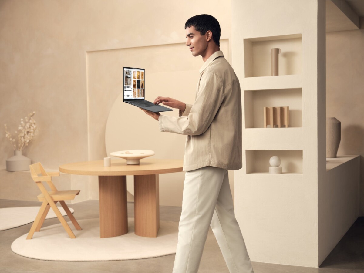 a man carrying an asus zenbook a14 laptop in a beige room